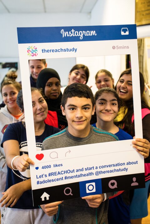 Picture of children holding a cutout frame of an Instagram post saying "REACH Study"