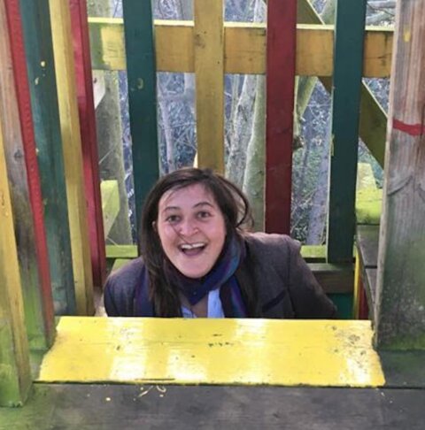 Photo of Hannah Cowan, in a children's playground, head and torso emerging as she climbs up a ladder onto a platform