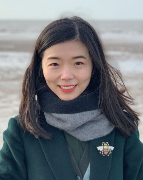 Jia Liu, in a jacket and scarf with a beach in the background