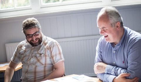 Two men sitting at a desk talking