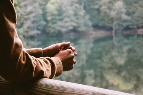 A person leans on a wooden rail, looking out over a lake and some trees