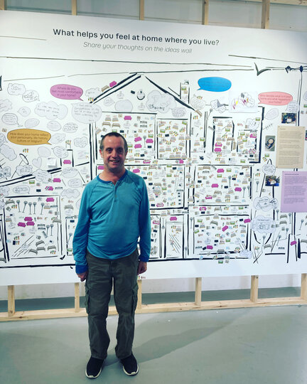 Photo of a man in a blue jumper standing in front of a poster about the research project