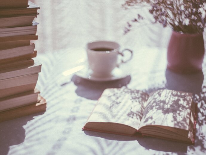 picture of a table with a vase of flowers, cup of tea, and an open book on it