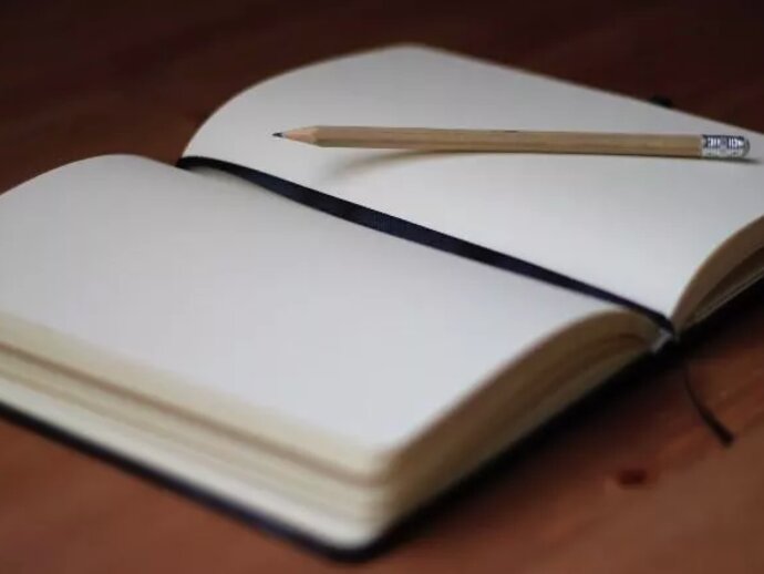 A notebook lying open, with blank pages and a yellow pencil on top