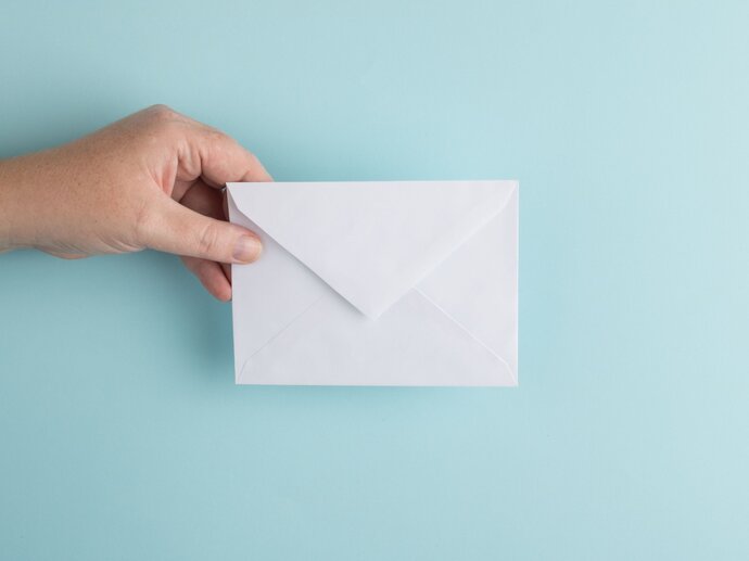 Picture of a hand holding a white envelope against a blue background