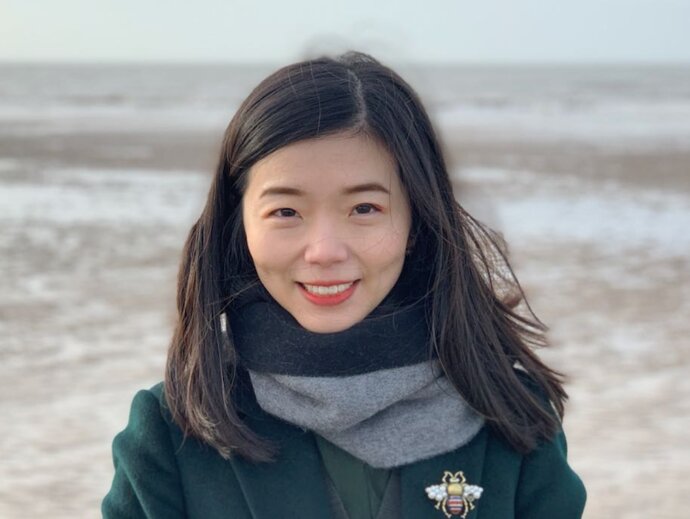 Jia Liu, in a jacket and scarf with a beach in the background