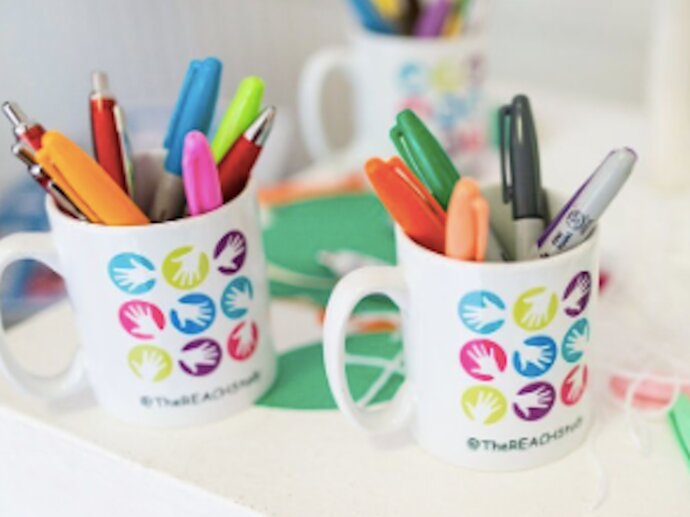 Photo of two mugs with the REACH study logo on them, and assorted pens inside