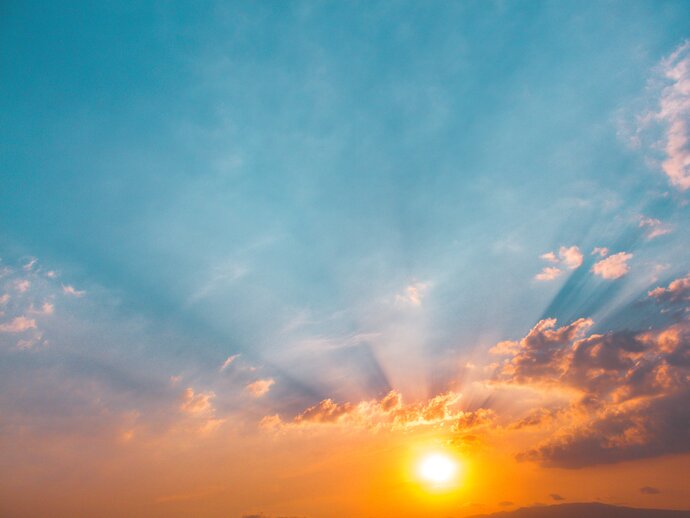 Photo of the sun rising, with sun rays showing through clouds