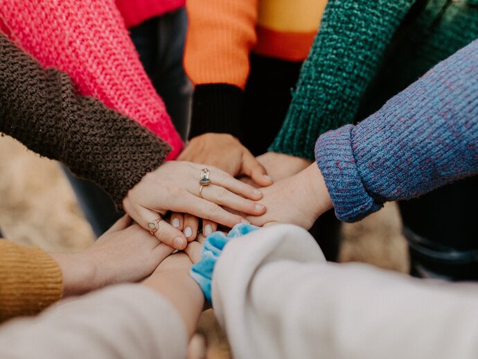 Hands from different people stacked on top of each other in a supportive circle