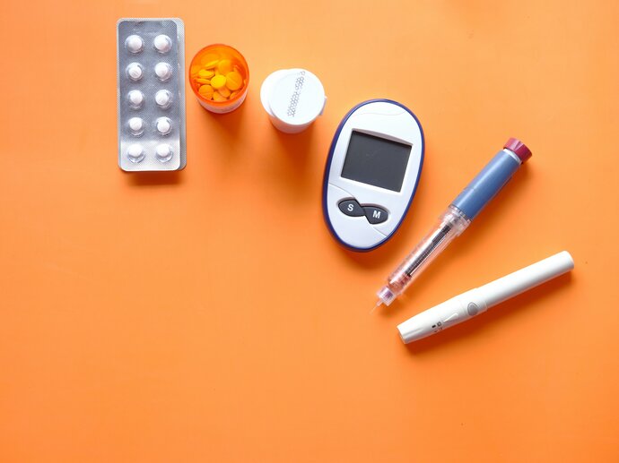 insulin pen, diabetic measurement tools and pills on orange background