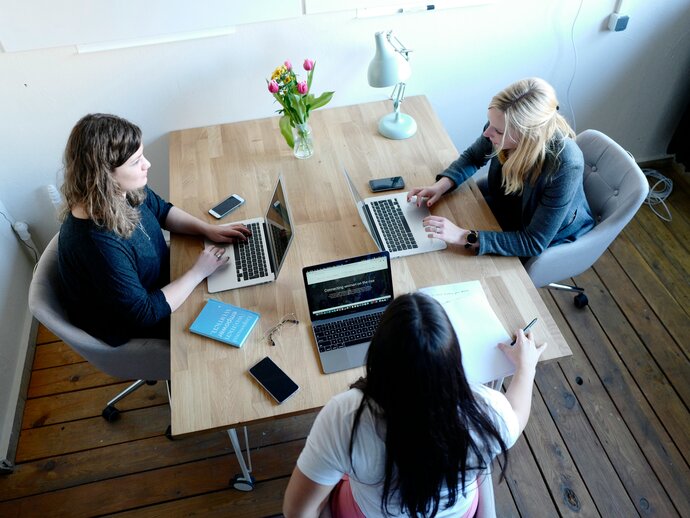 Three women sat around a table on their laptops
