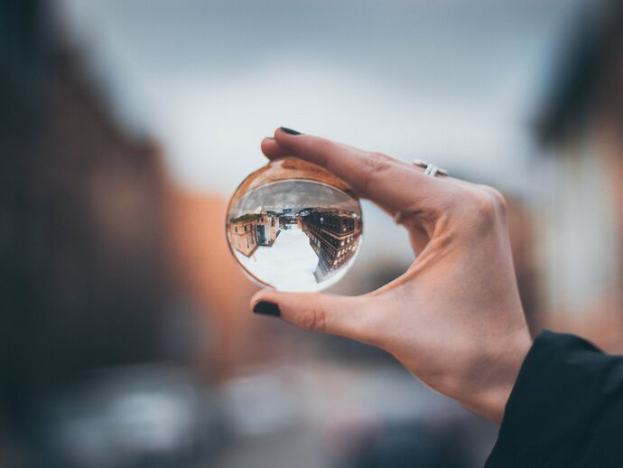 Picture of a hand holding a glass ball, which brings the blurred background into focus