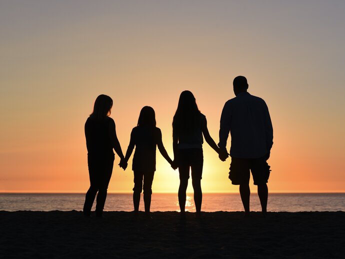 Photo of four people holding hands, silhouetted against the sunset on a beach