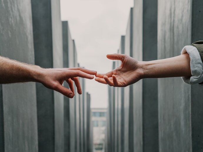 Two hands from different people reaching out to hold each other across an empty street