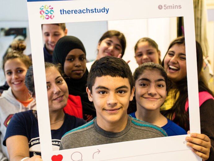 Picture of children holding a cutout frame of an Instagram post saying "REACH Study"