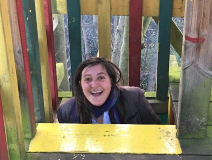 Photo of Hannah Cowan, in a children's playground, head and torso emerging as she climbs up a ladder onto a platform