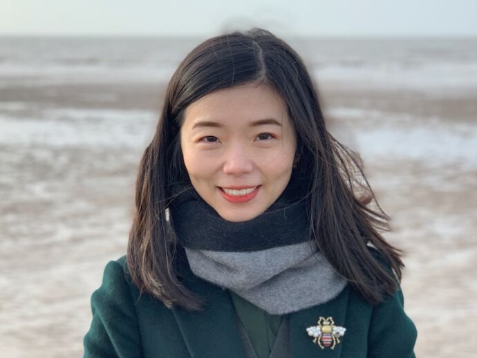 Jia Liu, in a jacket and scarf with a beach in the background