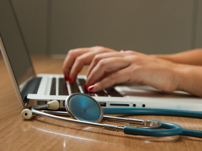 hands typing on a laptop, with a stethoscope on the table in the foreground