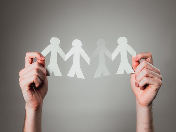 Co-production A pair of hands holds up paper cutouts of four figures joined together holding hands