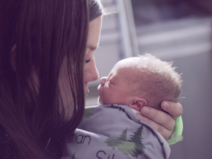 A woman holds a tiny baby close to her face, nose to nose. The baby is swaddled in a green cloth.