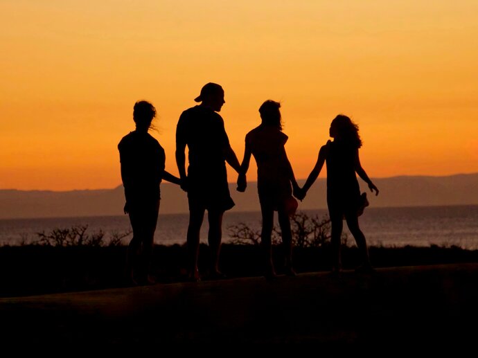 A family of four - two parents and two children - are silhouetted against an orange sunset