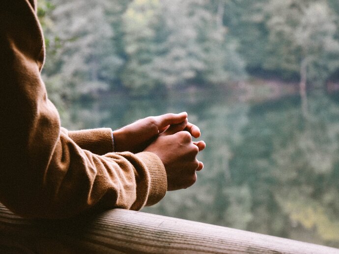 A person leans on a wooden rail, looking out over a lake and some trees