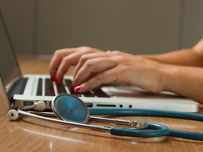 A stethoscope lies next to a laptop with someone typing on it