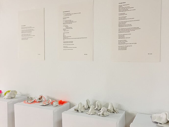 photo of a piece from the exhibition: poetry exhibited on the wall above small ghost-like sculptures on plinths