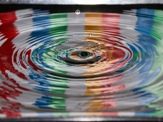 A rainbow coloured photo of a drop of water falling in a pond