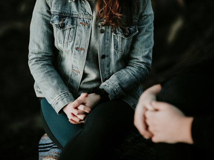 two people sitting opposite each other with hands folded on their laps