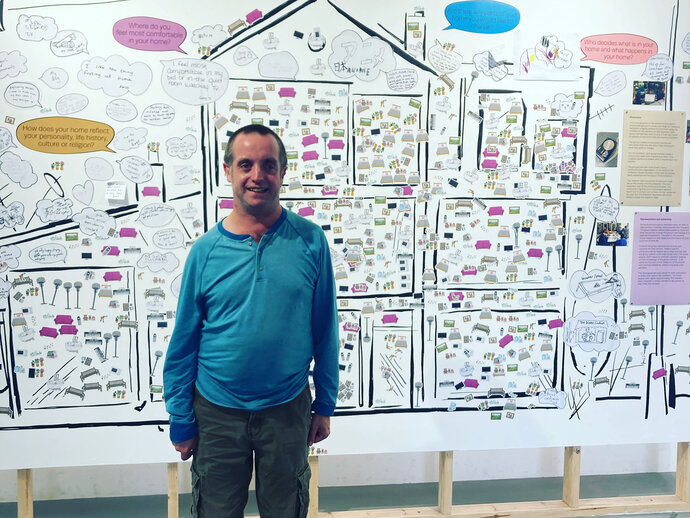 Photo of a man in a blue jumper standing in front of a poster about the research project