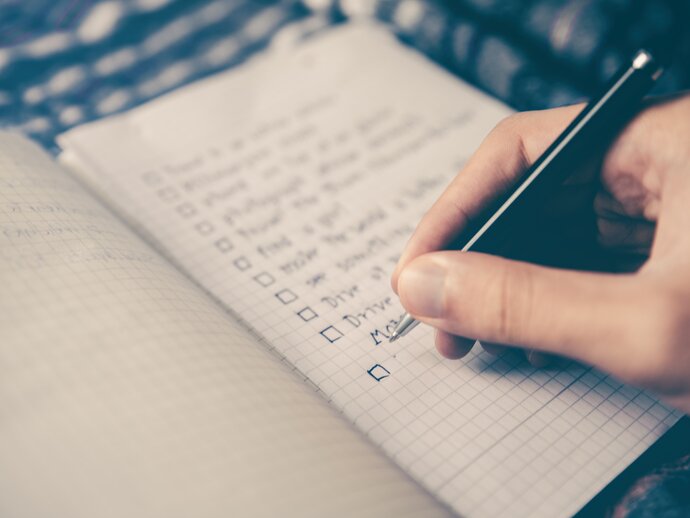 A hand holding a pen ticks off an item on a checklist in a notebook