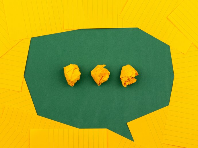 Yellow paper arranged to shape a speech bubble on a green background, with three dots in the speech bubble
