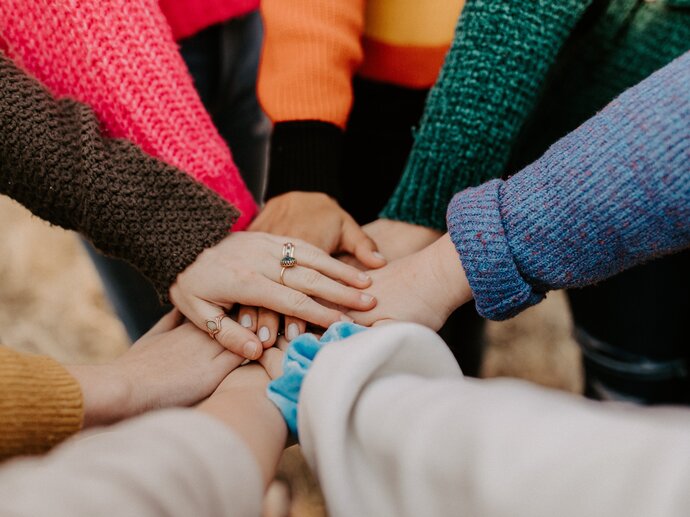 Arms and hands in a circle with hands of a group of people stacked on top of each other - 'all in'