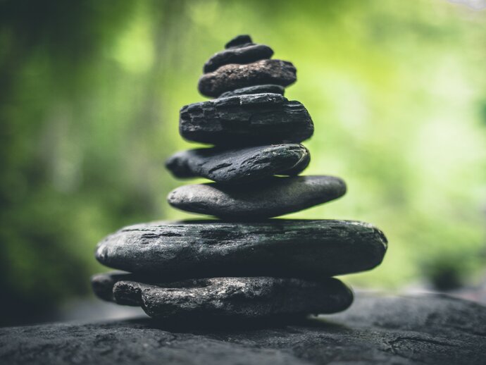 A pile of pebbles, balanced one on top of another from large at the bottom to small at the top, against a green, leafy background