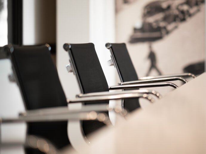 Close up shot of a row of black, smart chairs lined up along a table, evocative of a committee meeting