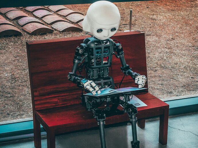 Image by Andrea de Santis via Unsplash A cute little humanoid robot holding a digital book