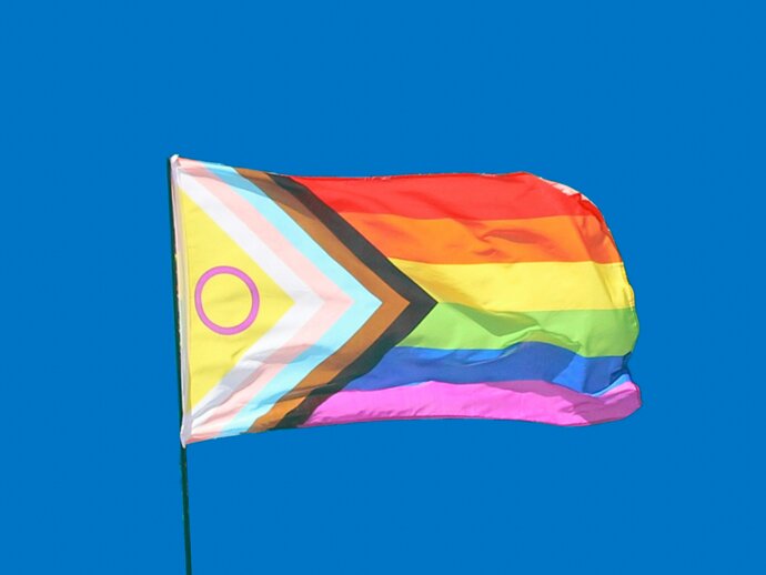 a progress pride flag flying in a bright blue sky