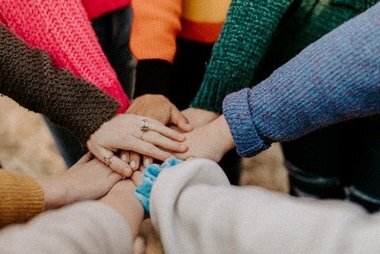 Hands from different people stacked on top of each other in a supportive circle