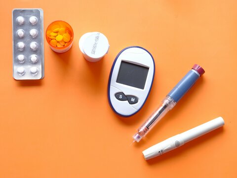 insulin pen, diabetic measurement tools and pills on orange background