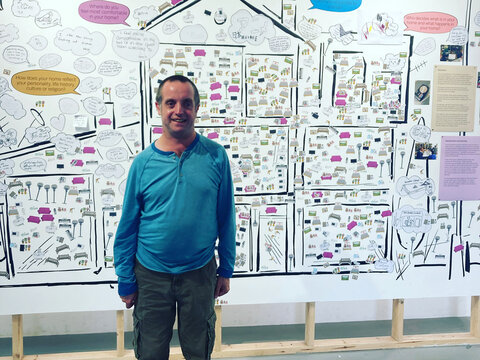 Photo of a man in a blue jumper standing in front of a poster about the research project