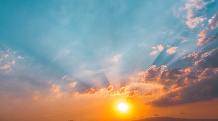 Sun rising through clouds, beams of light shining through the clouds