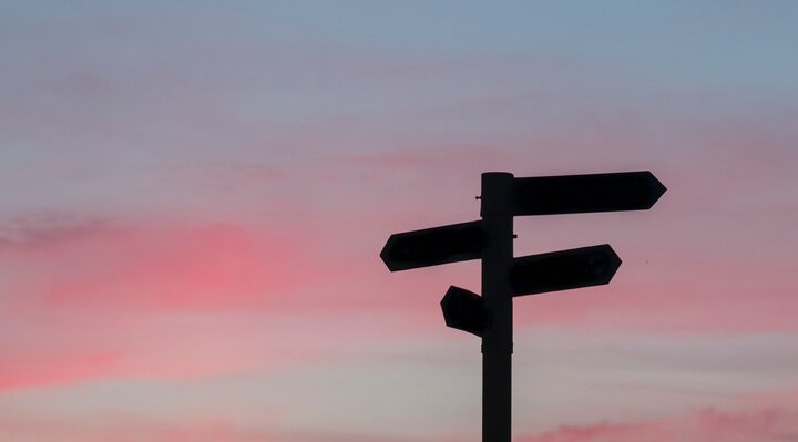 Signpost with three signs pointing different directions, silhouetted against a pink and blue sky