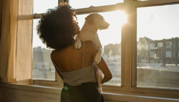 Black woman standing at a window holding a small dog
