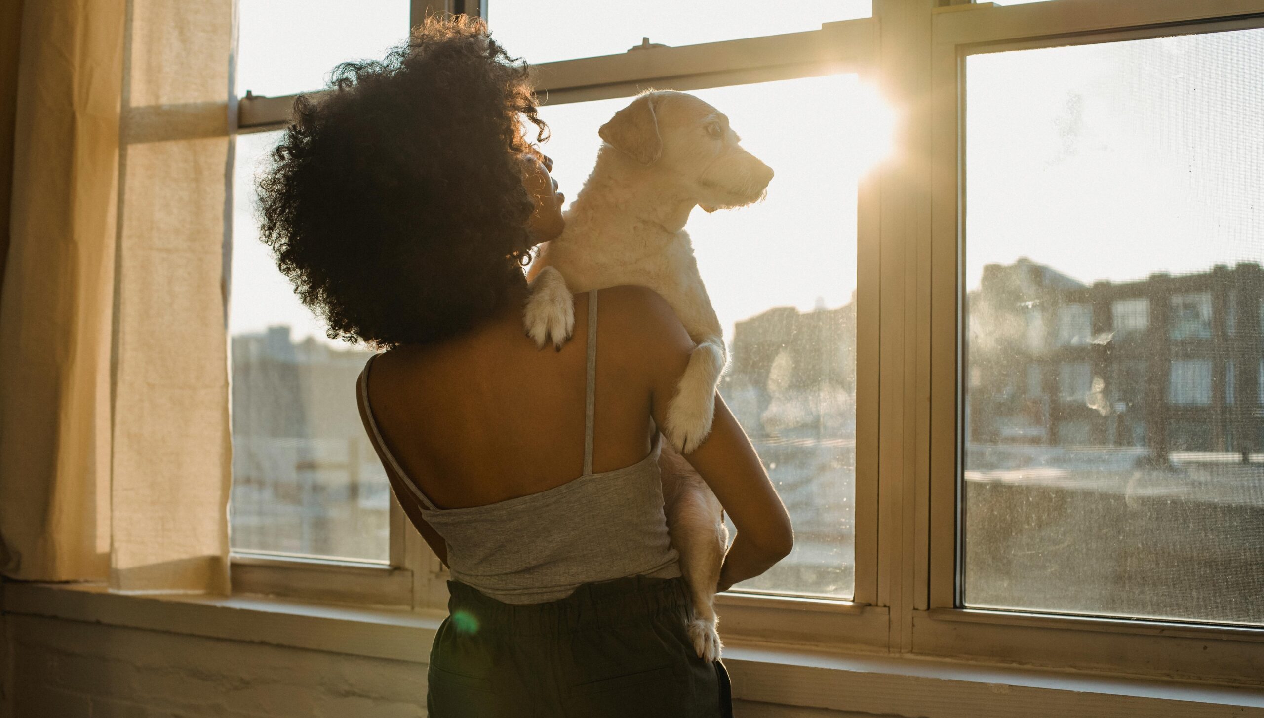 Black woman standing at a window holding a small dog