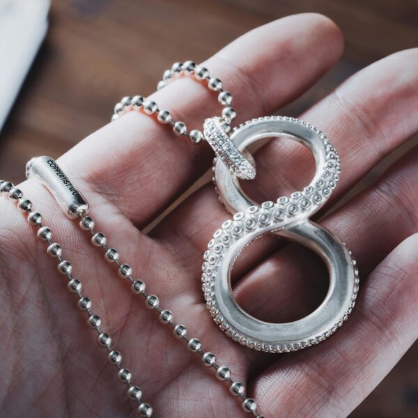 A necklace in the shape of the infinity symbol made out of tentacles, held in someones hand