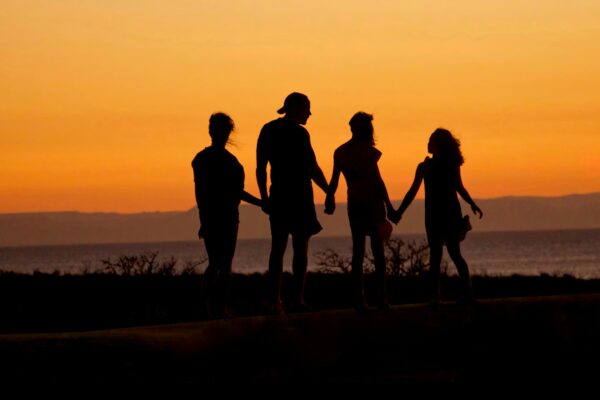 A family of four - two parents and two children - are silhouetted against an orange sunset