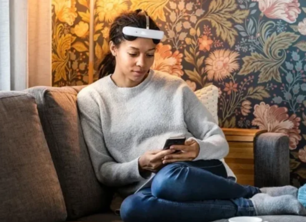 A woman on the sofa looking at her phone with a TCDS device on her head