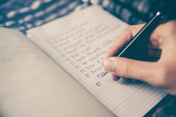 A hand holding a pen ticks off an item on a checklist in a notebook