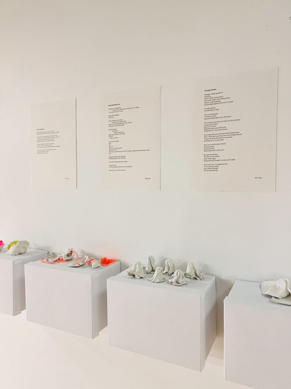 photo of a piece from the exhibition: poetry exhibited on the wall above small ghost-like sculptures on plinths